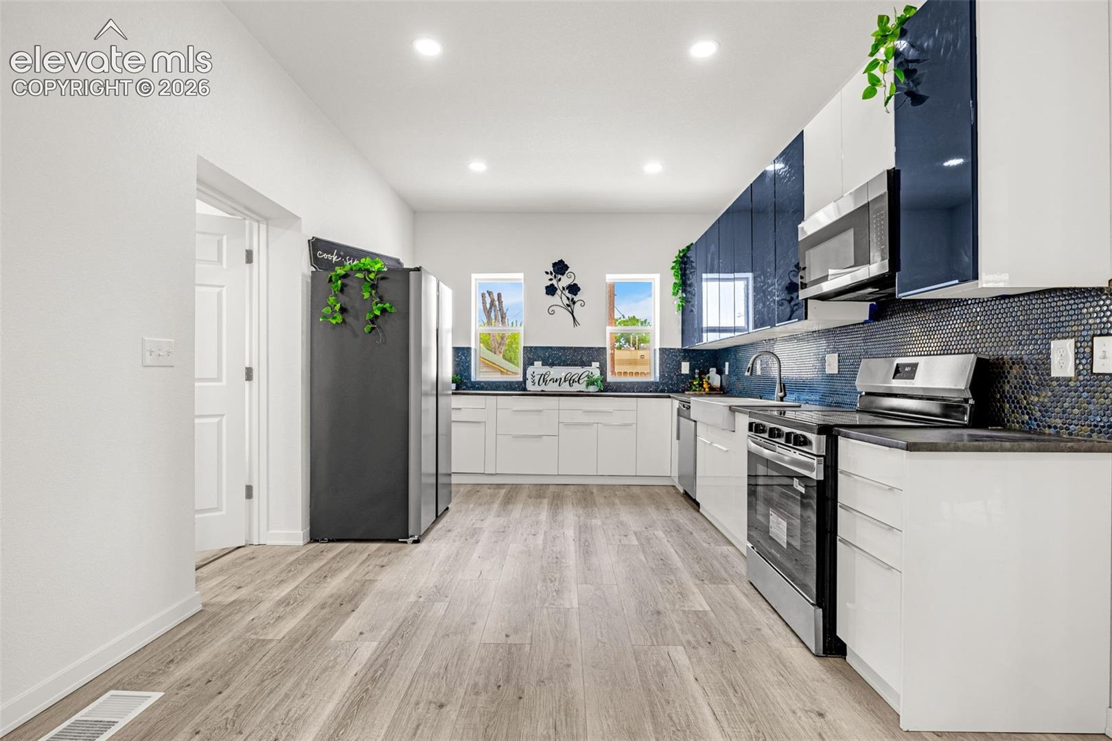 Modern kitchen featuring sleek white cabinetry, a stylish blue mosaic tile backsplash, stainless steel appliances, and light wood-finish flooring