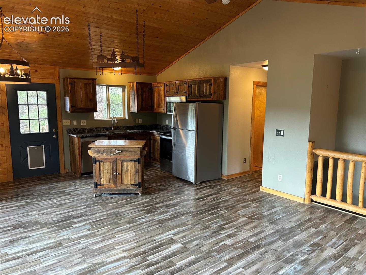 Kitchen featuring rustic wood cabinetry, wood-finish flooring, vaulted wood-paneled ceilings, stainless steel appliances, and a log-style balustrade