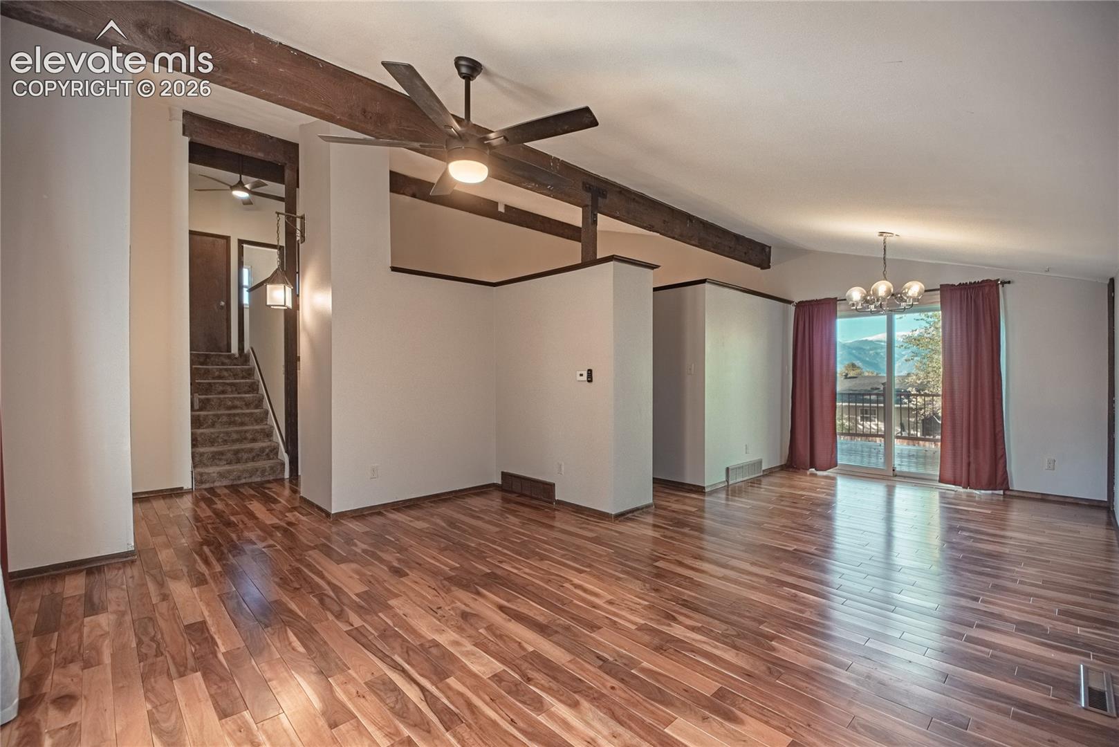 Vaulted ceiling with exposed wood beams, wood-finish flooring, ceiling fan, and sliding glass doors
