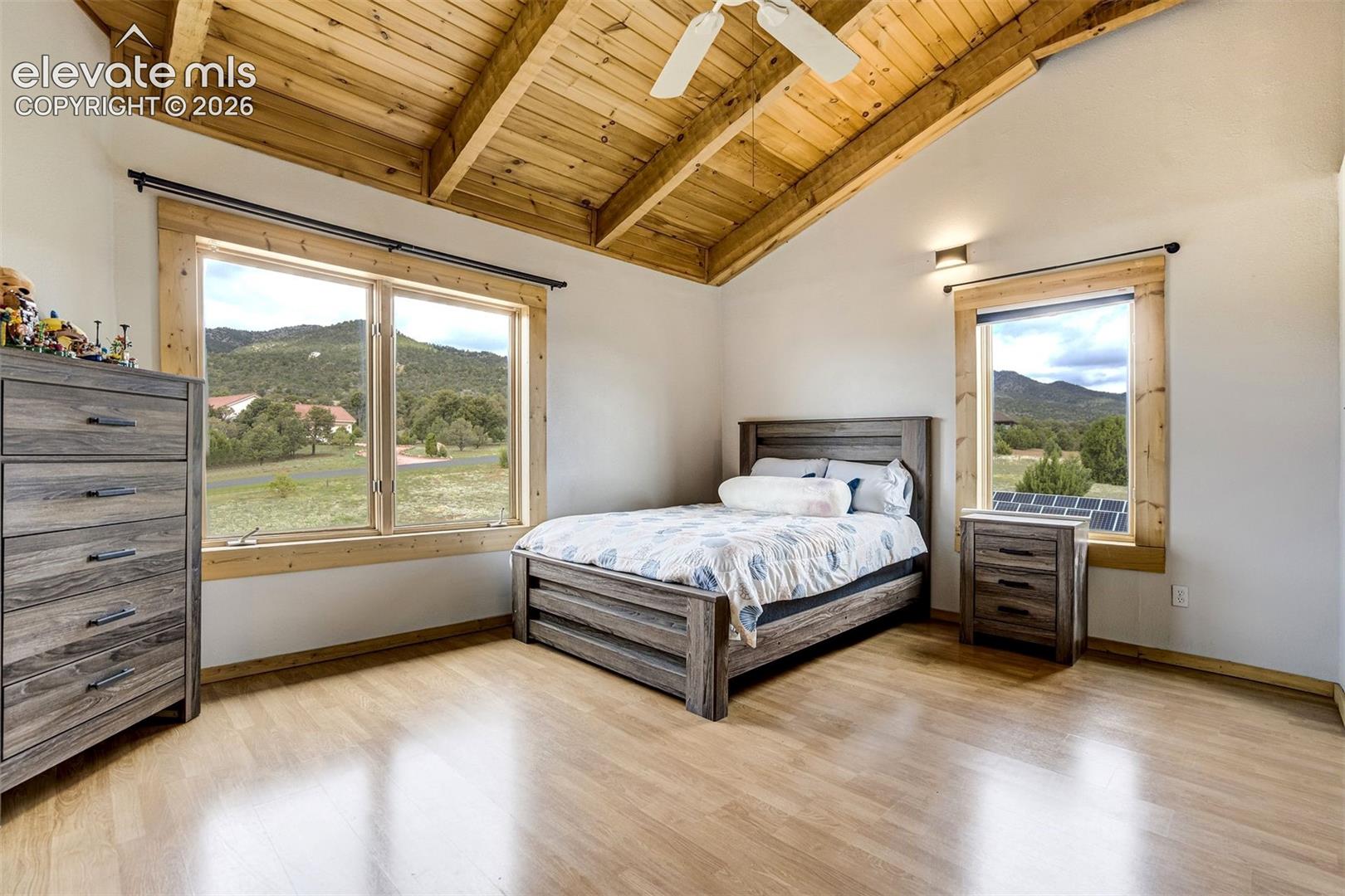 Room featuring a vaulted wood-finish ceiling with exposed beams, wood-finish flooring, and white walls