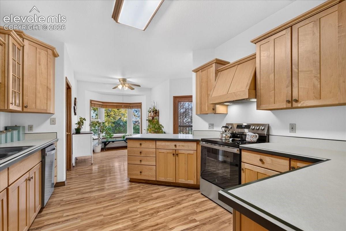 Kitchen featuring natural wood cabinetry, stainless steel range, wood-finish flooring, recessed skylight, and a bay window