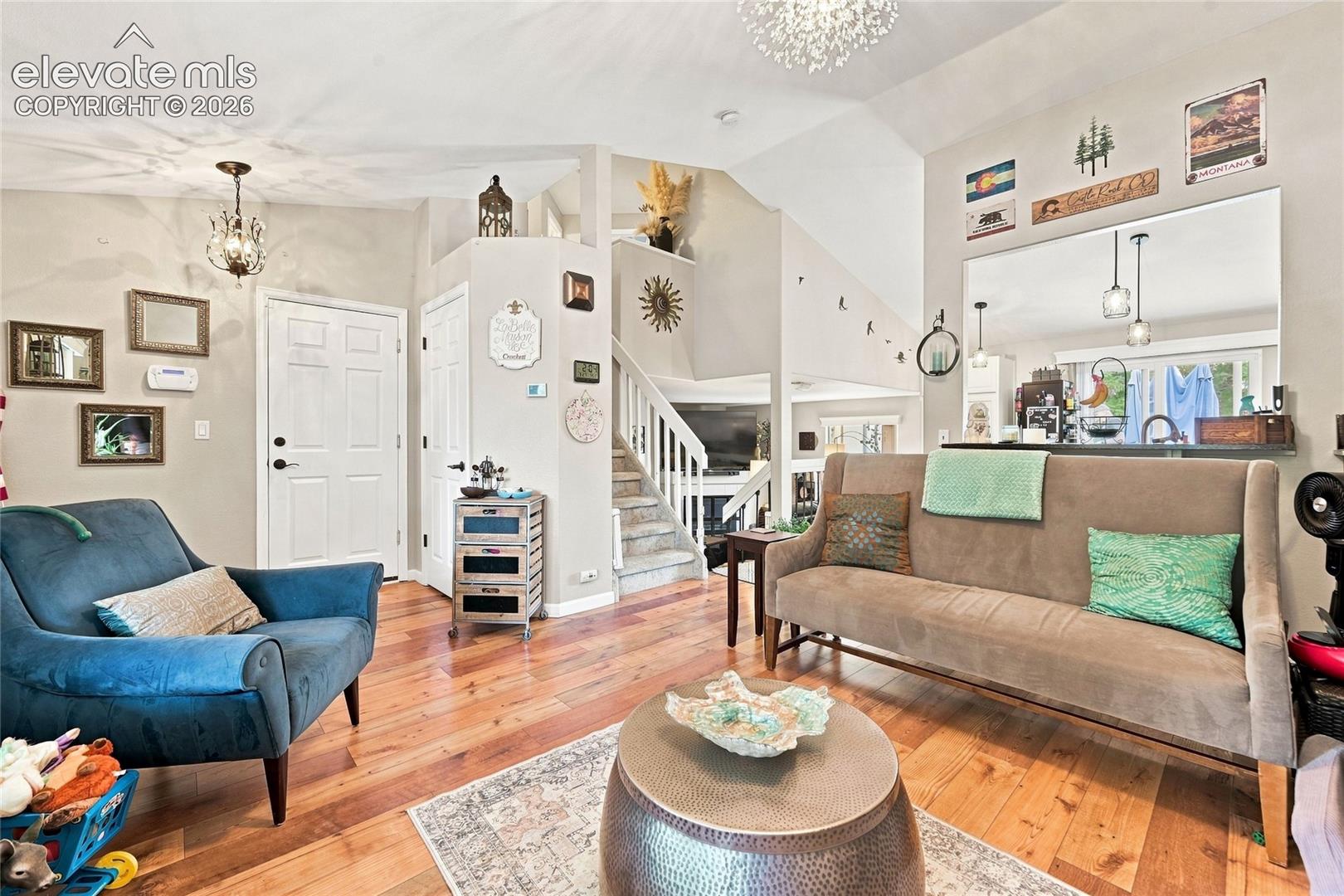 Living area featuring vaulted ceilings, wood-finish flooring, a staircase with white balusters, and a pass-through opening