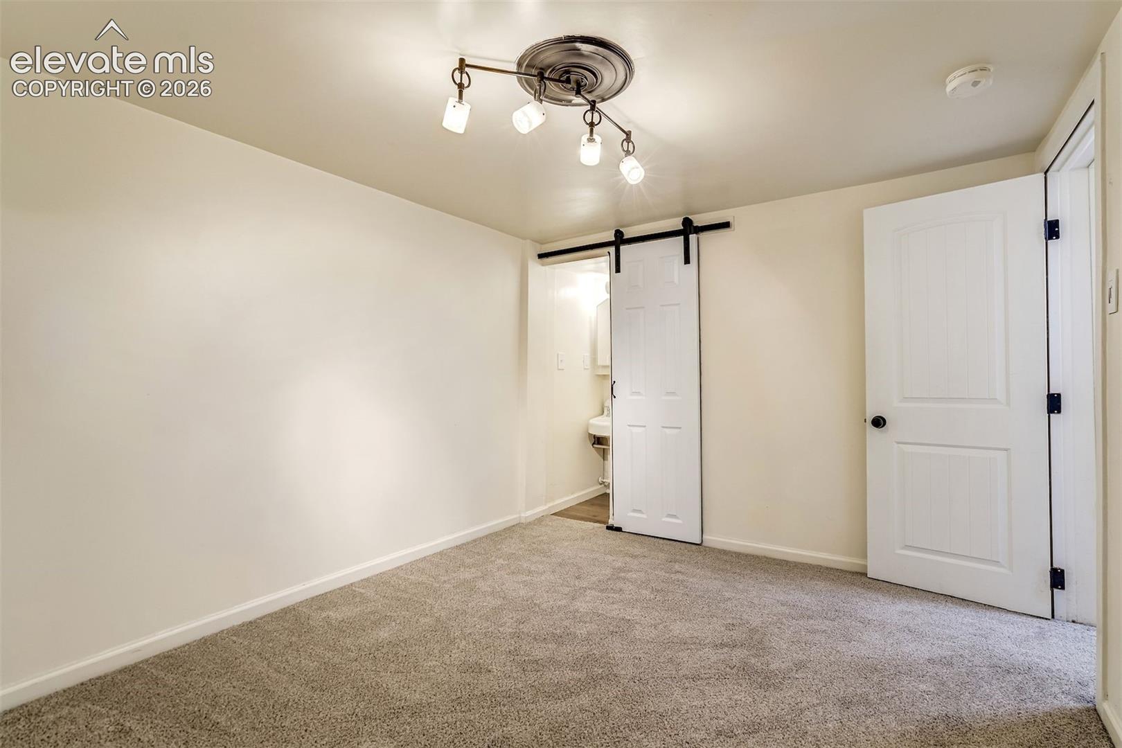 Interior space featuring wall-to-wall carpeting, a multi-light track fixture with a decorative ceiling medallion, and a white sliding barn door with black hardware