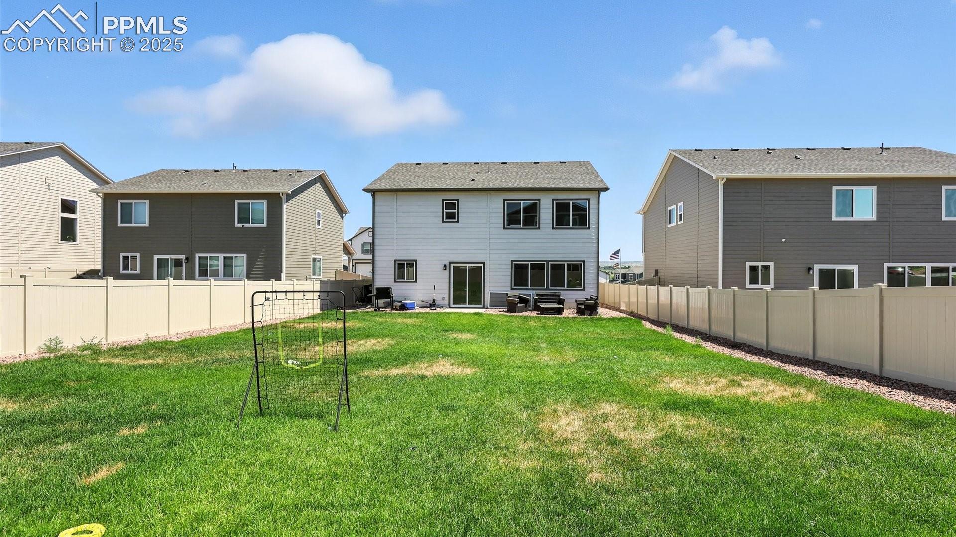 Spacious fenced backyard with concrete patio, rock beds, and lush green grass.