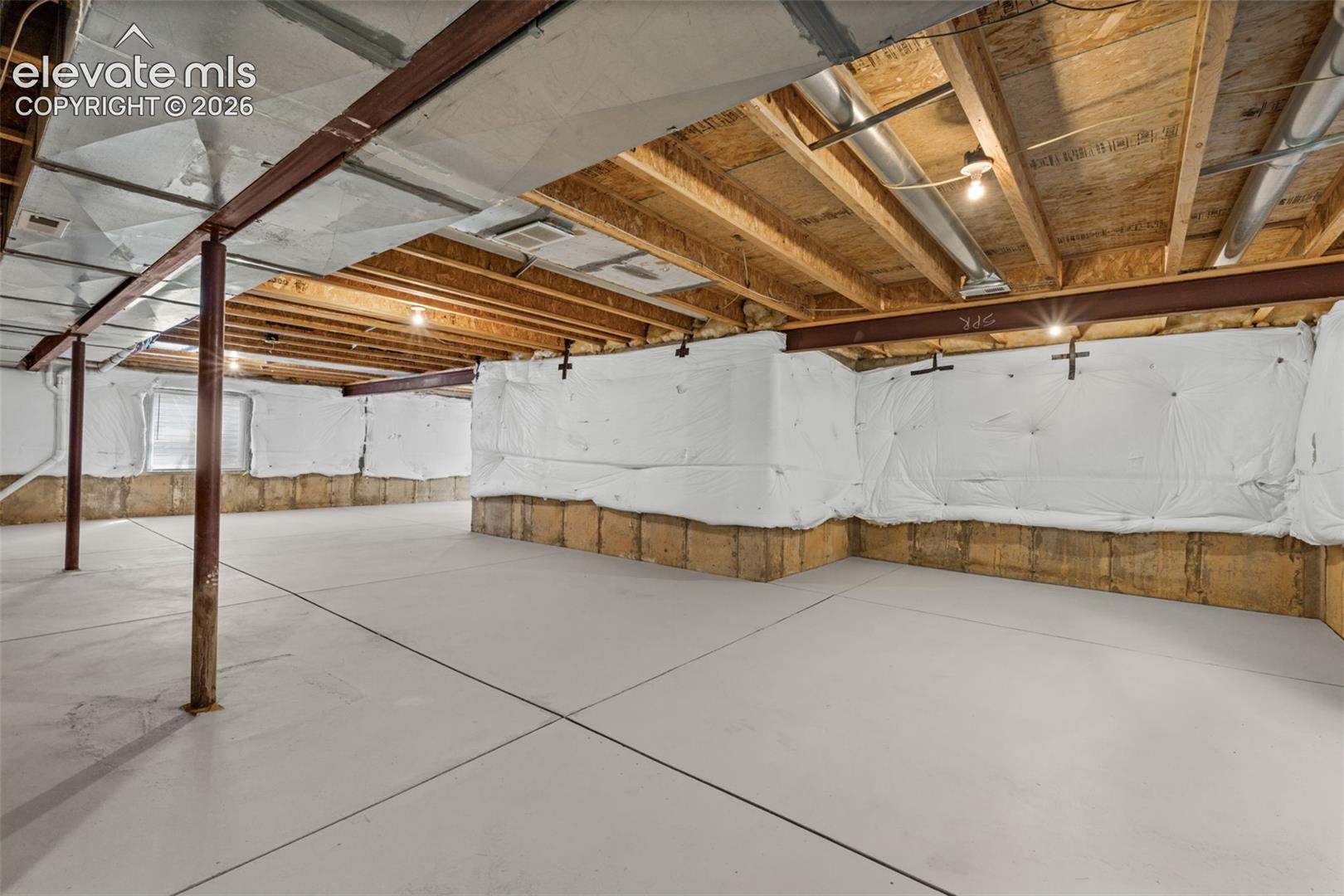 Unfinished lower level featuring smooth concrete flooring, exposed wood ceiling joists, steel support columns, and insulated foundation walls