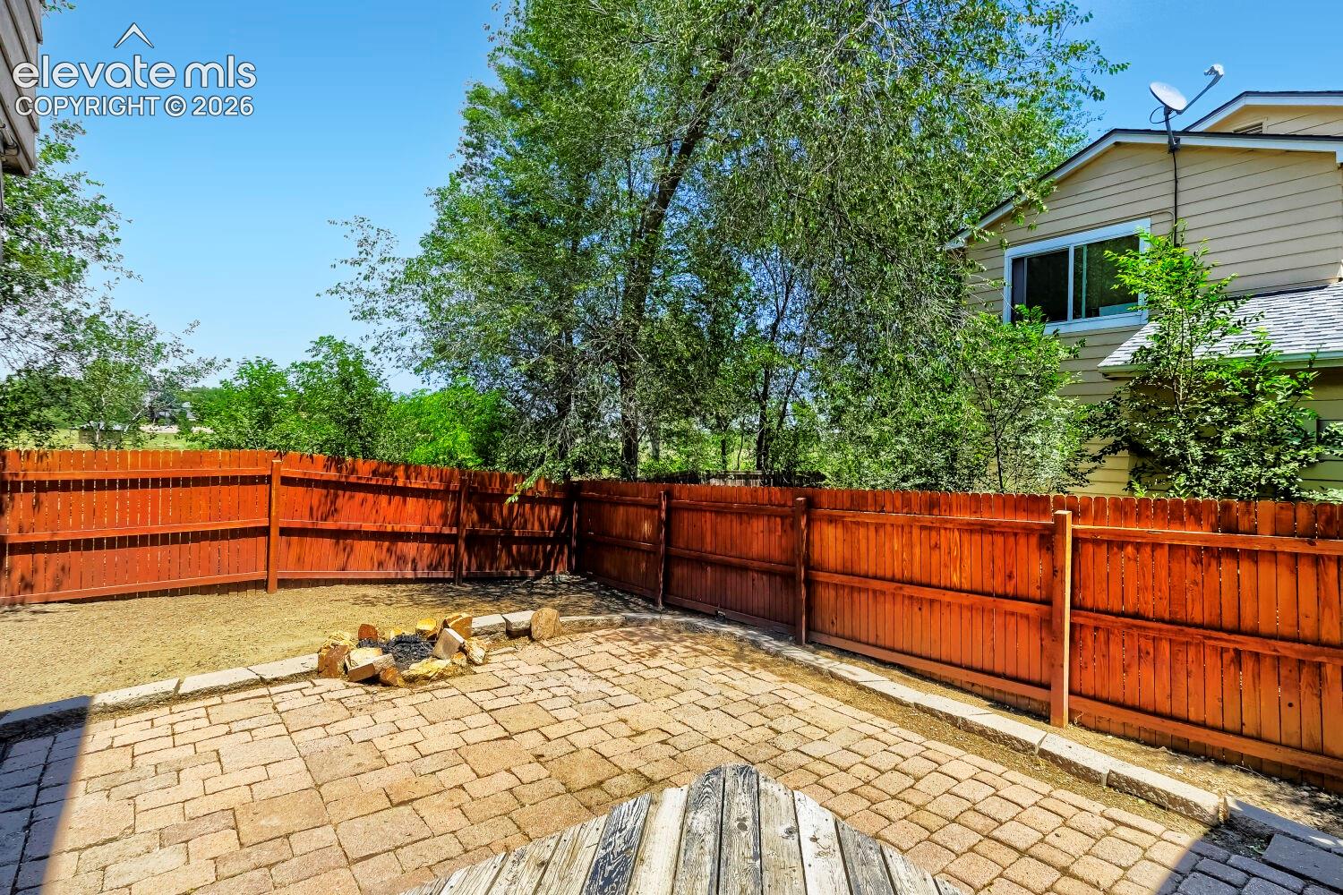 Expansive backyard featuring a paver patio with a stone fire pit, wood privacy fencing
