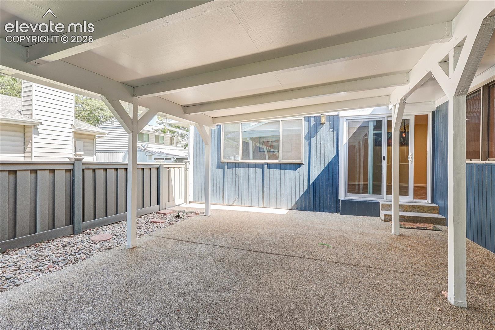 Covered patio featuring a textured concrete surface, white structural support beams, vertical exterior siding, and a fenced perimeter