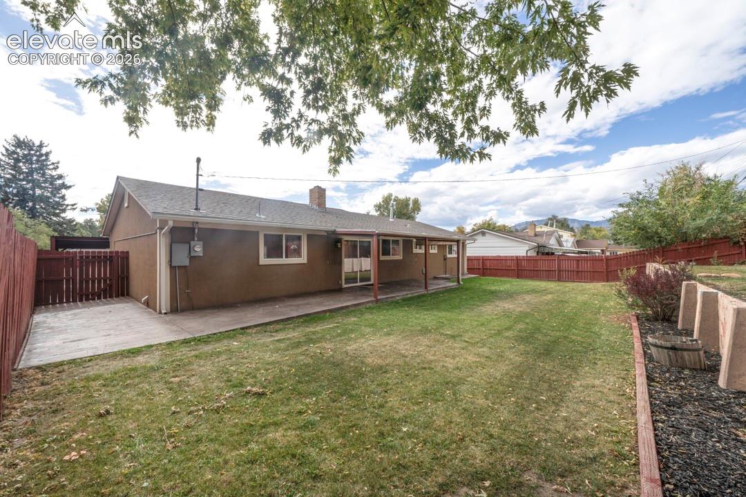 Private backyard featuring a sprawling lawn, covered patio, full-height wood fencing, and terraced landscaping with concrete retaining walls