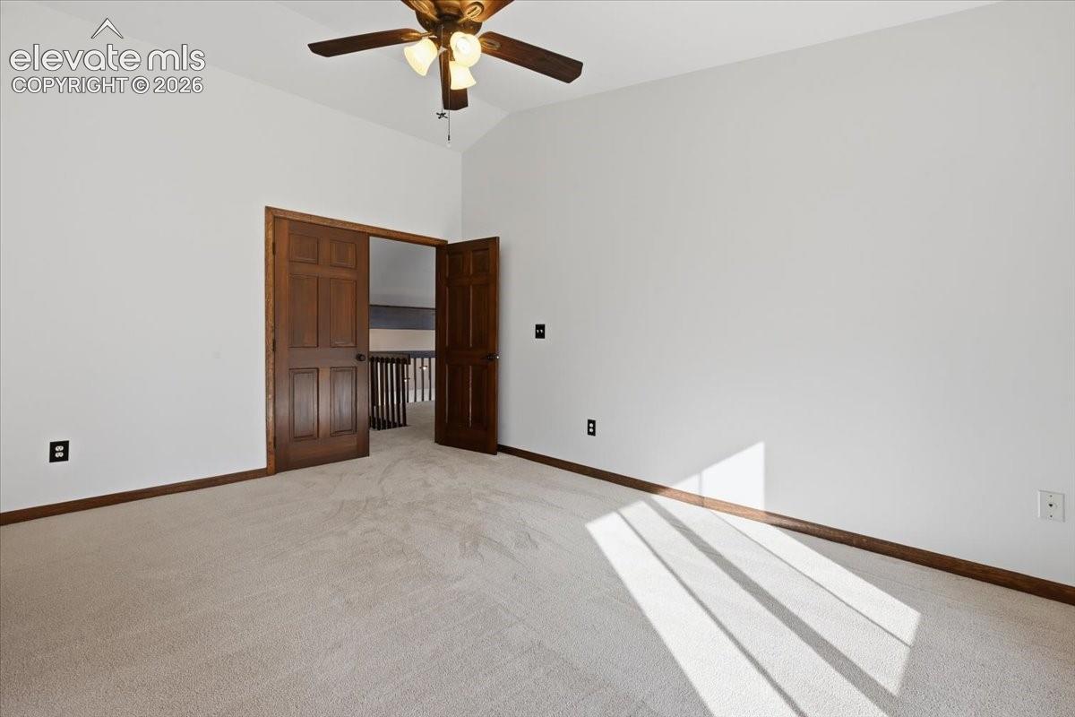 Vaulted ceiling featuring a ceiling fan with integrated lighting, wood-finish bi-fold doors, white walls, and neutral carpeting
