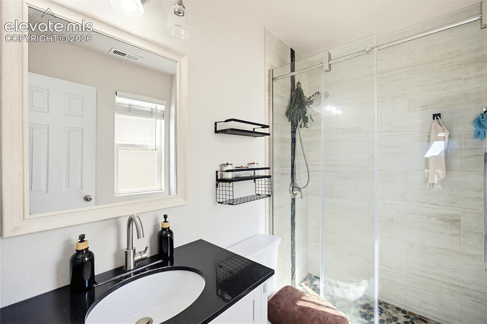 White framed mirror, dark countertop vanity, modern faucet, glass-enclosed shower, and tiled shower walls