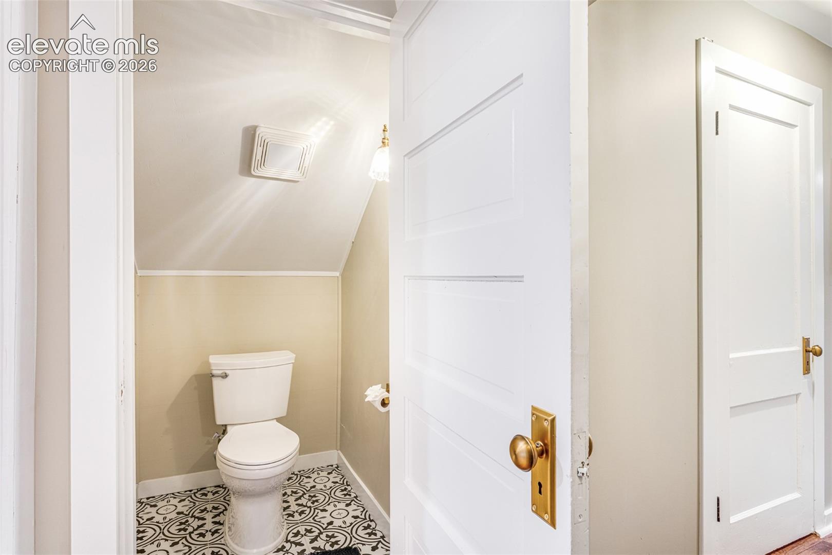 Compact powder room featuring a patterned tile floor, white toilet, and beige wall paint