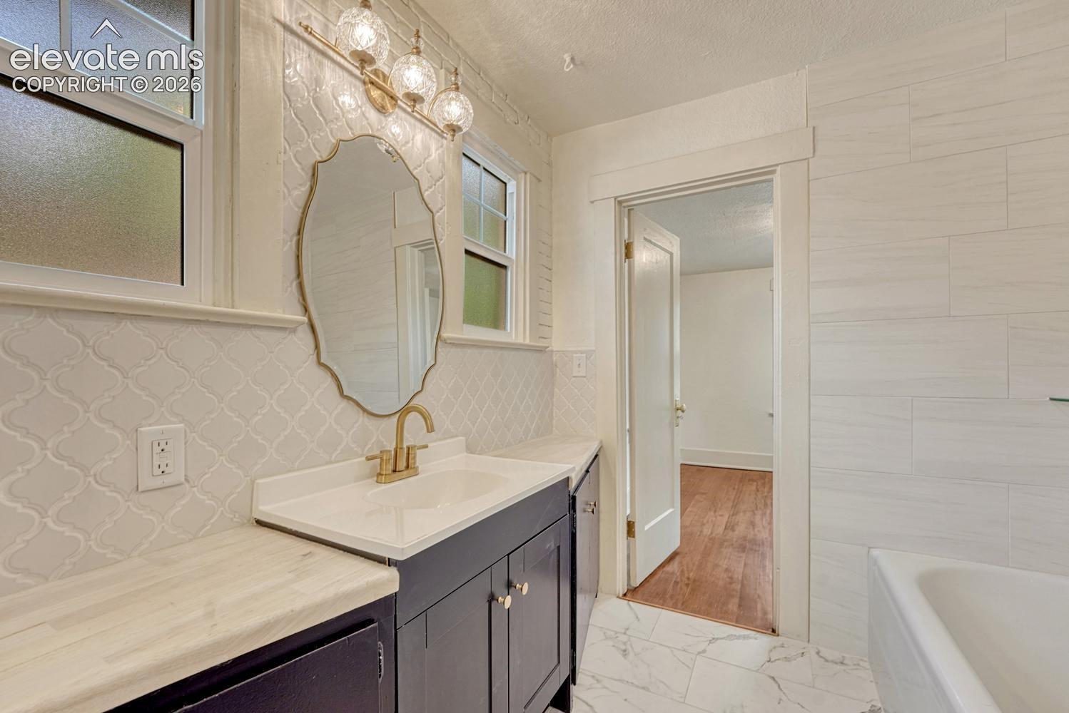 White tile wainscoting and flooring, dark wood-finish vanity with a white countertop, and brass-finish faucet