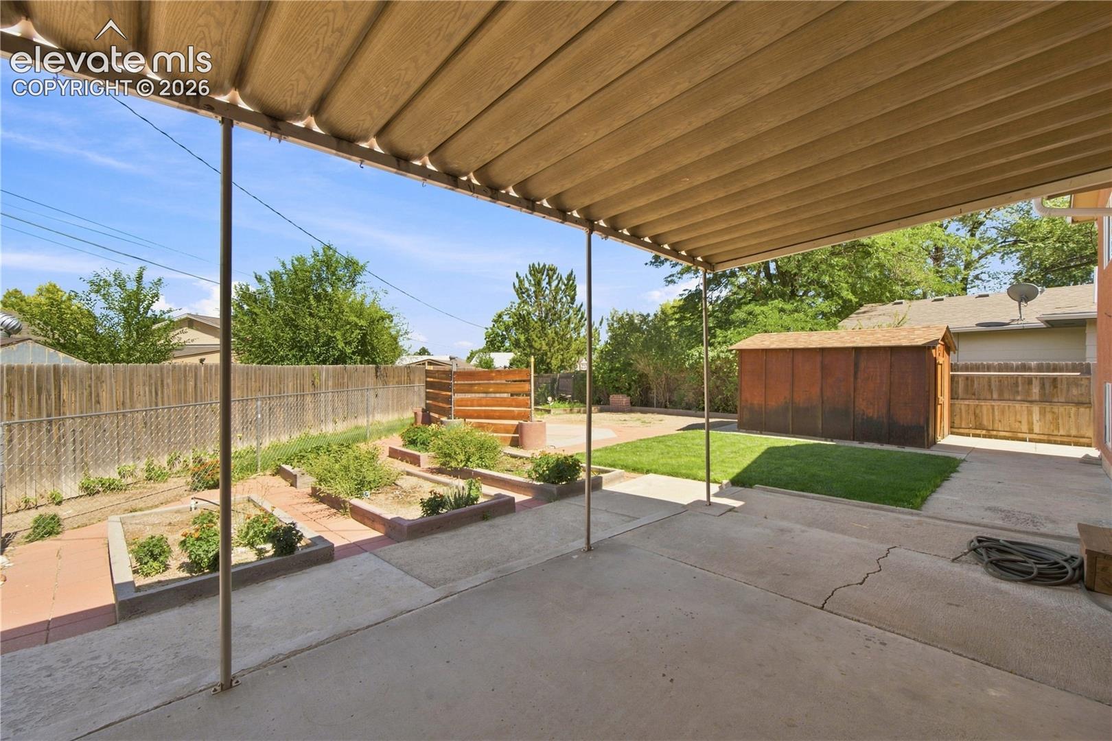 Covered patio with concrete flooring, raised garden beds, and a storage shed