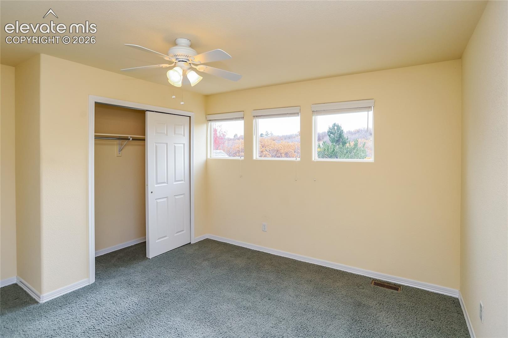 Room featuring wall-to-wall carpeting, a ceiling fan with integrated lighting, a walk-in closet with built-in shelving, and three high-set windows