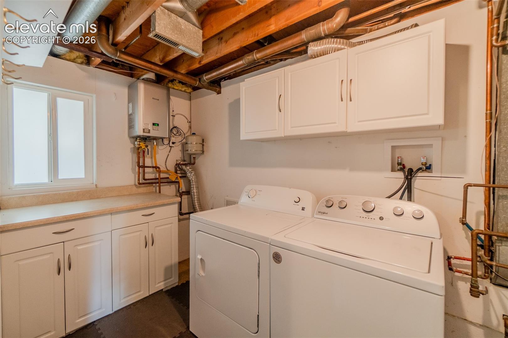 Laundry area featuring white cabinetry, a light-toned countertop, and a window