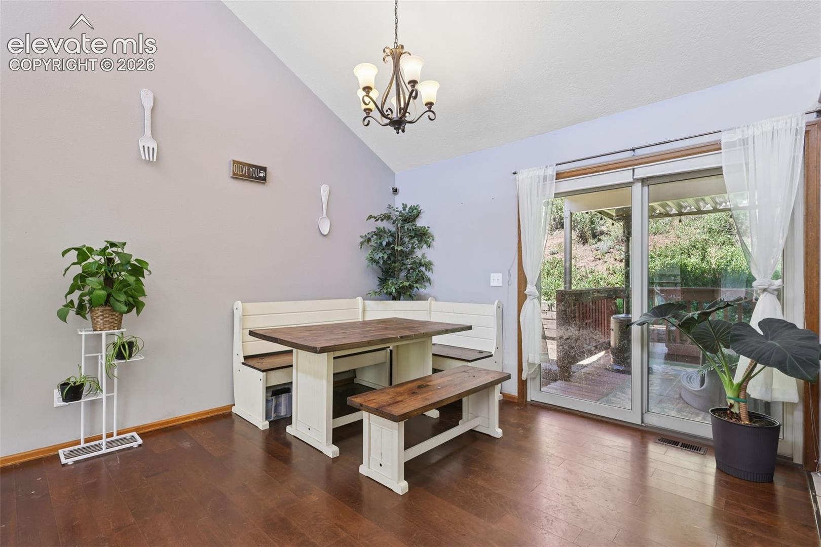 Vaulted ceiling with an ornamental chandelier, wood-finish flooring, and sliding glass door