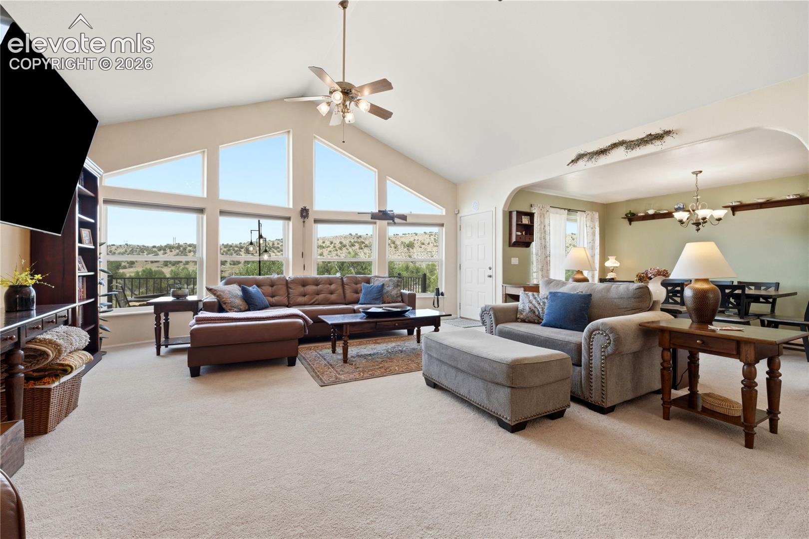 Vaulted ceiling with a ceiling fan, expansive windows, built-in shelving, and light-toned carpeting throughout