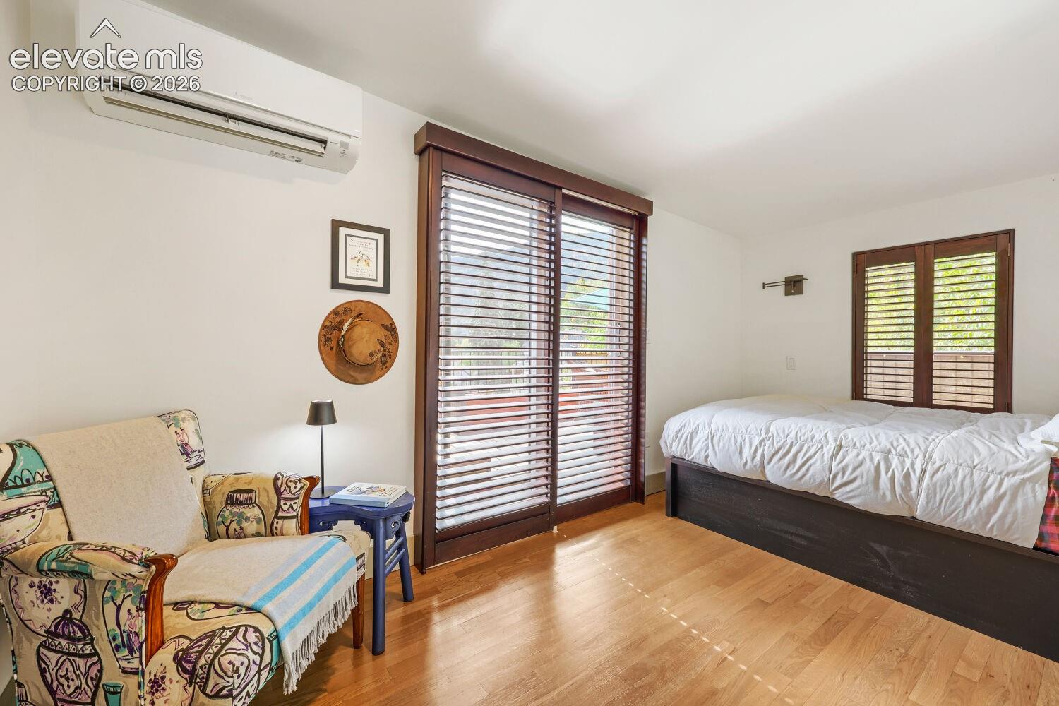 Wood-finish flooring, wall-mounted air conditioning unit, and wood-framed glass sliding doors with blinds