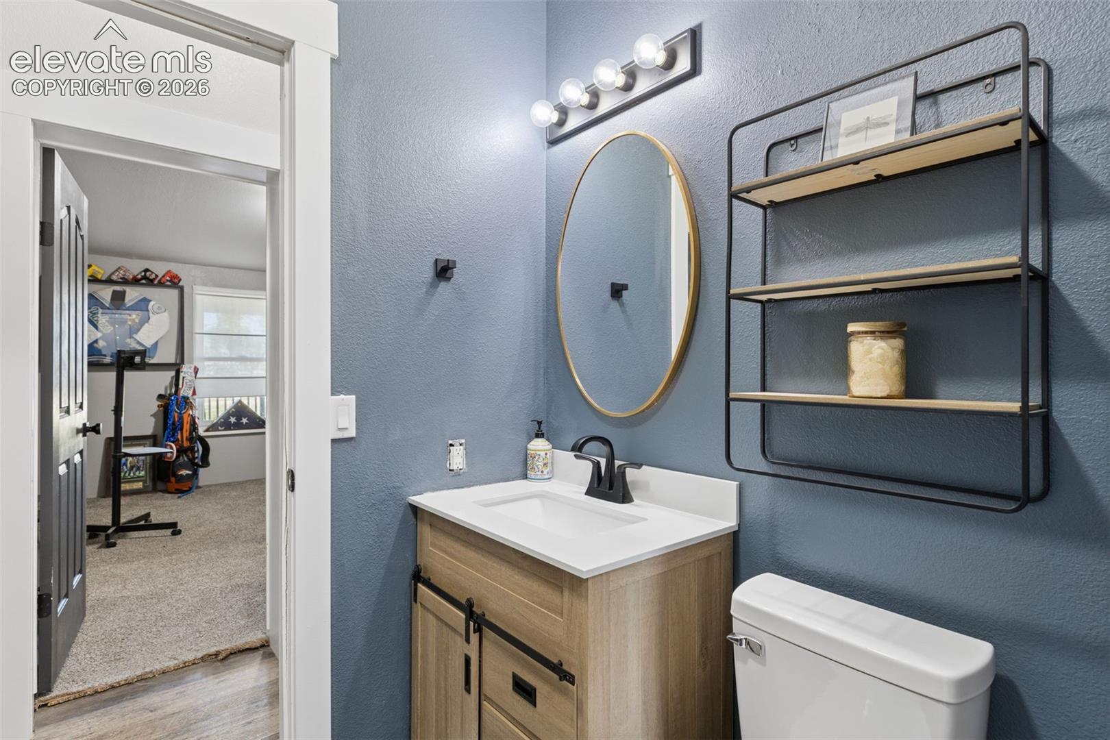 Bathroom featuring a wood-finish vanity with a rectangular sink, matte black faucet, oval wall-mounted mirror, and multi-bulb light fixture