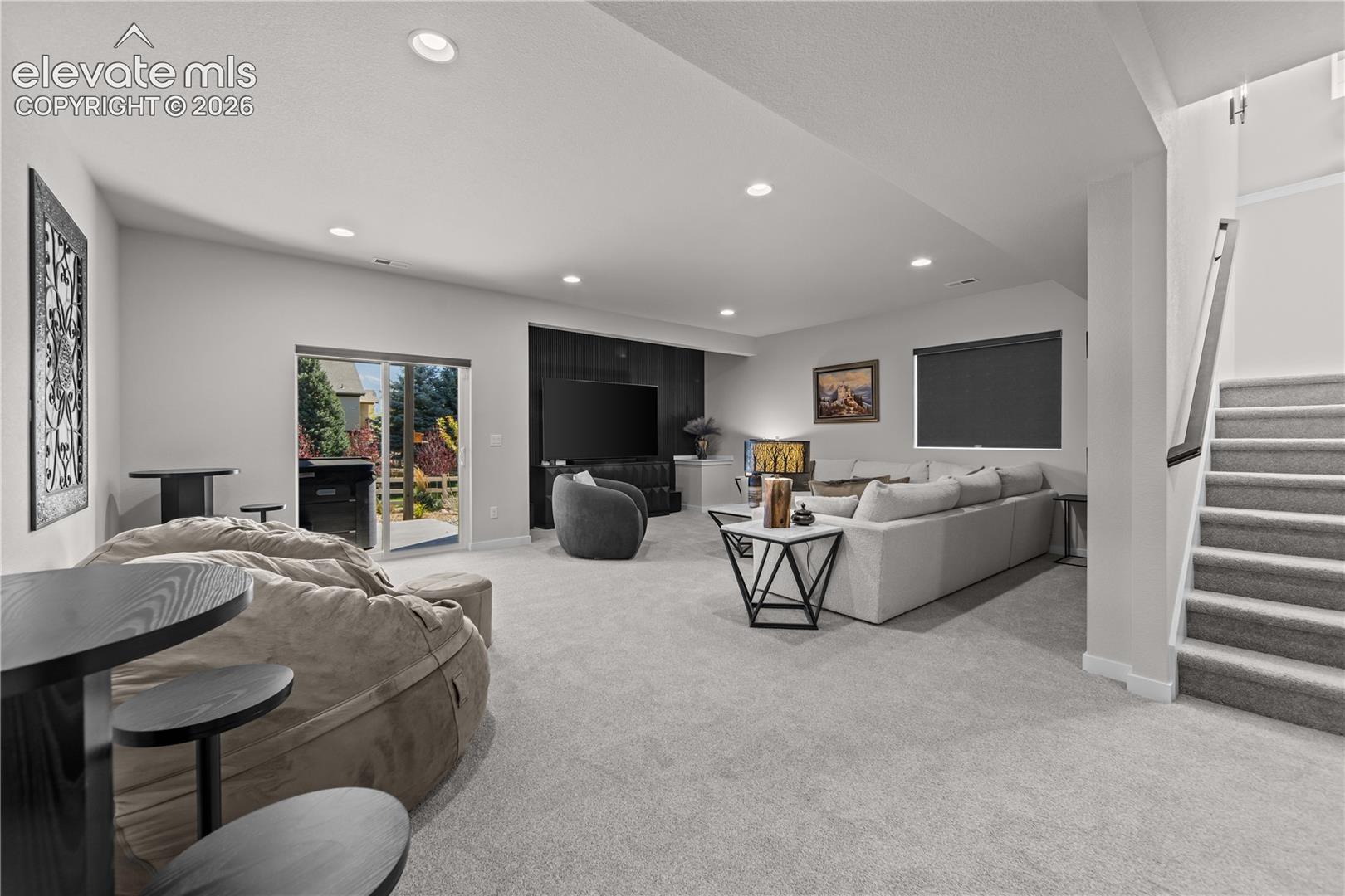 Open-concept living space featuring recessed lighting, wall-to-wall carpeting, a floor-to-ceiling dark accent wall, and a sliding glass door providing exterior egress