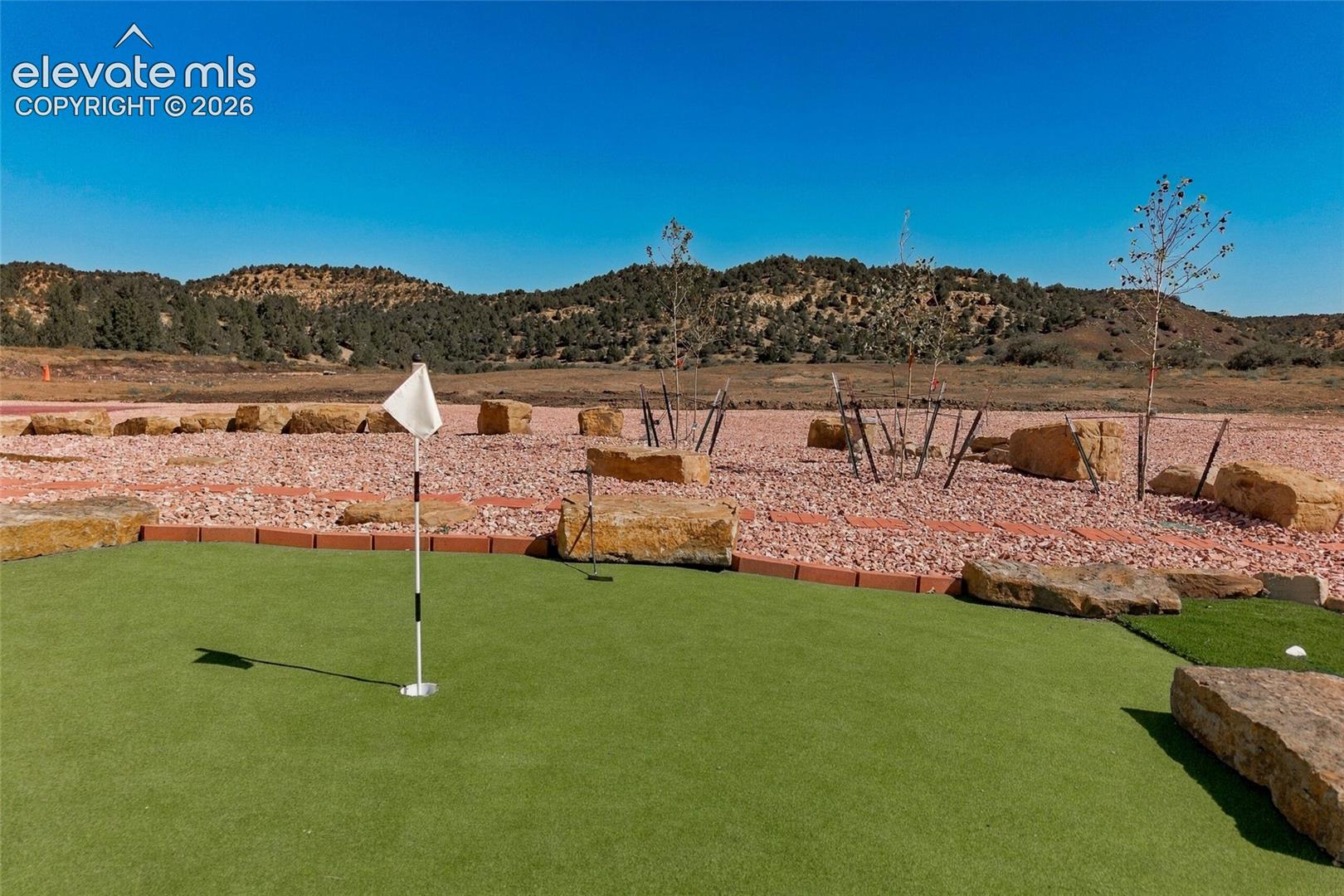 Artificial turf putting green with flagstick, surrounded by decorative red gravel and natural stone boulders