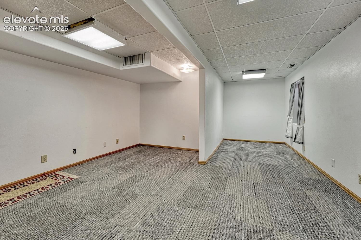 Carpeted flooring, white painted walls, and drop ceiling with integrated lighting