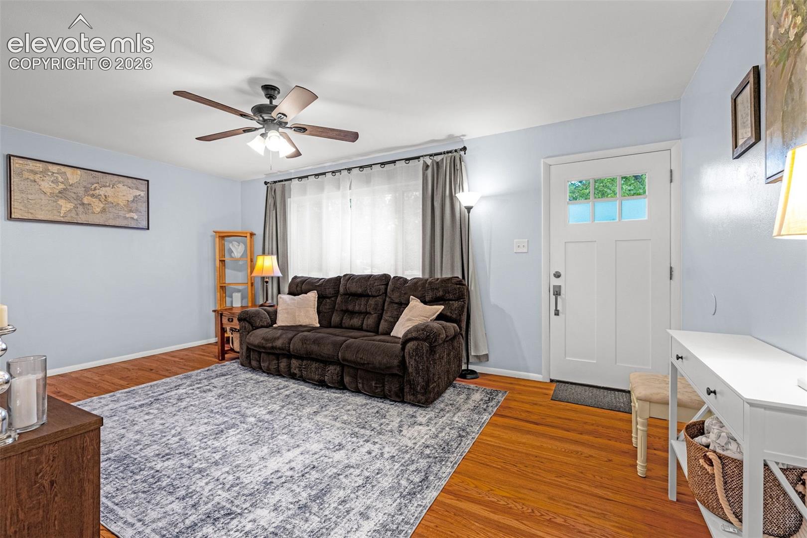 Hardwood flooring throughout, a white paneled entry door with glass, and a ceiling fan with integrated lighting