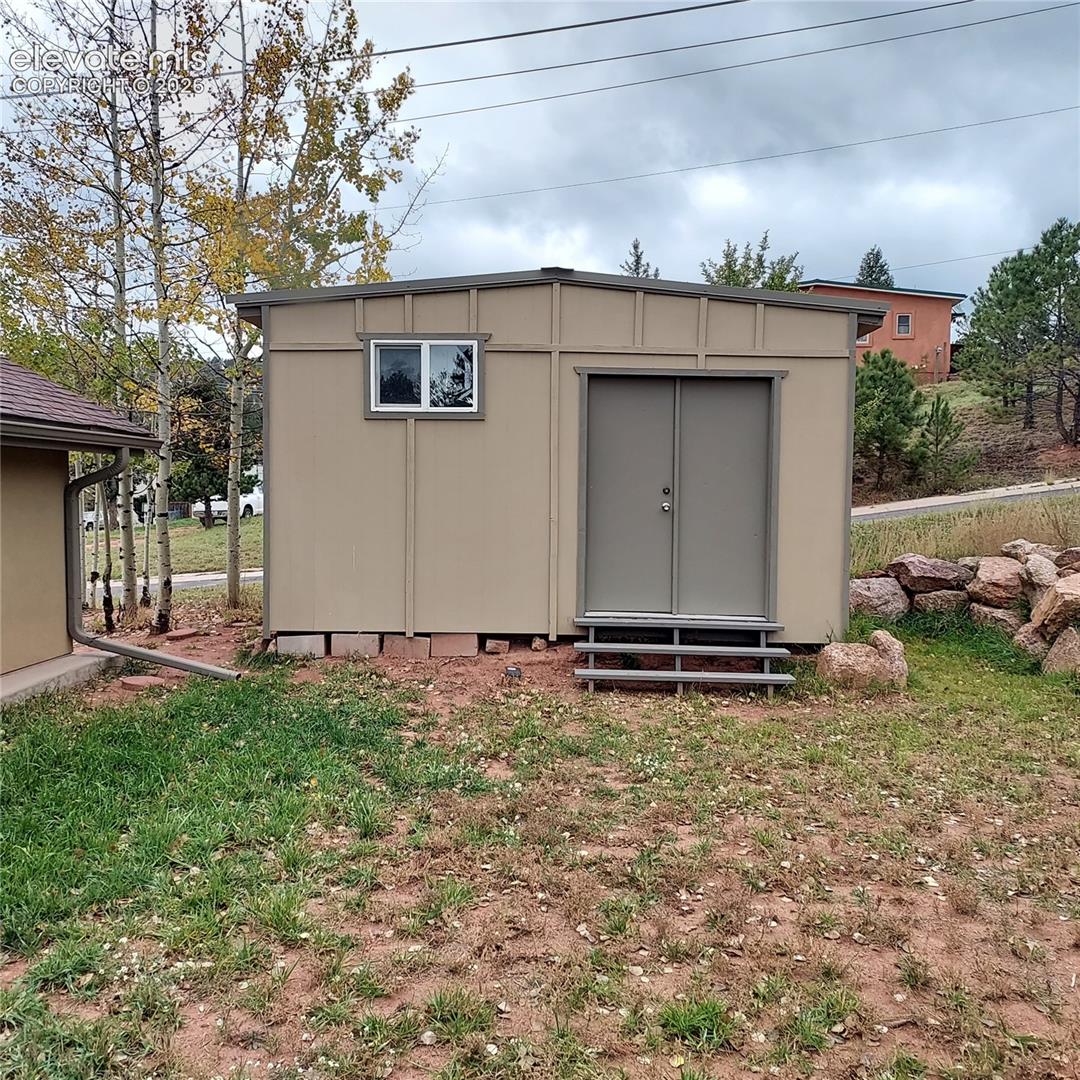 Detached storage structure featuring panel siding, double-door entry, a single rectangular window, and integrated stair access
