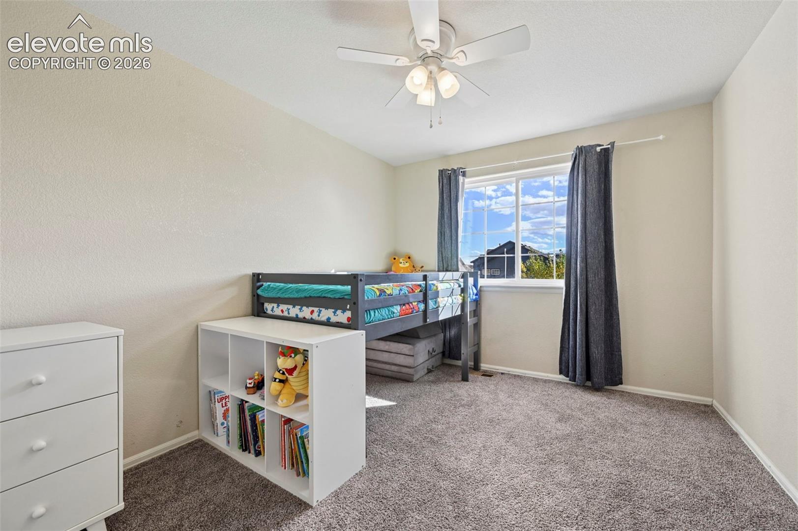 Neutral-toned interior featuring wall-to-wall carpeting, a multi-pane sliding window, and a white ceiling fan with integrated light fixture