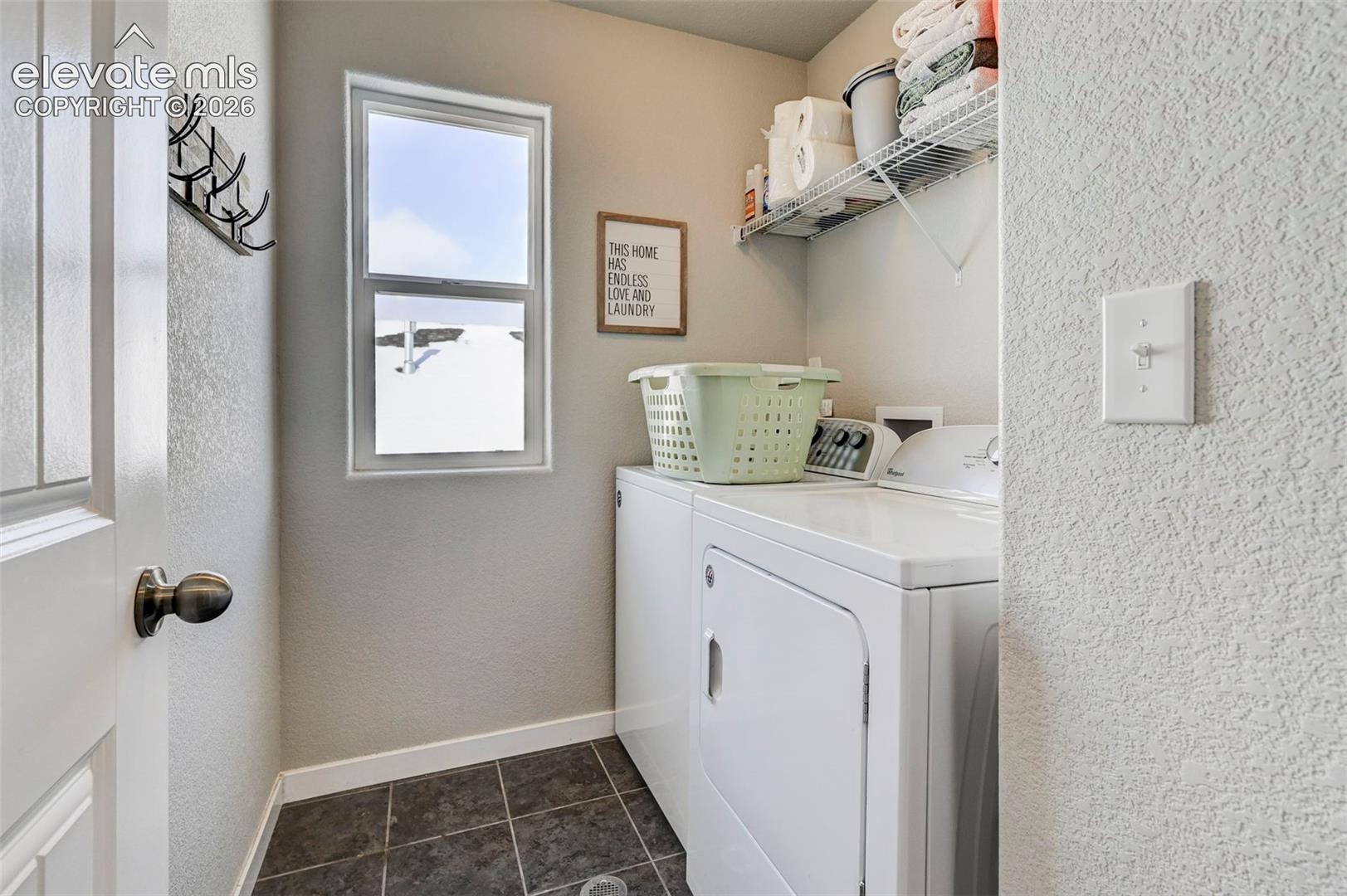 Laundry area featuring dark tile flooring, a vertical window, wall-mounted metal coat hooks, and wire shelving