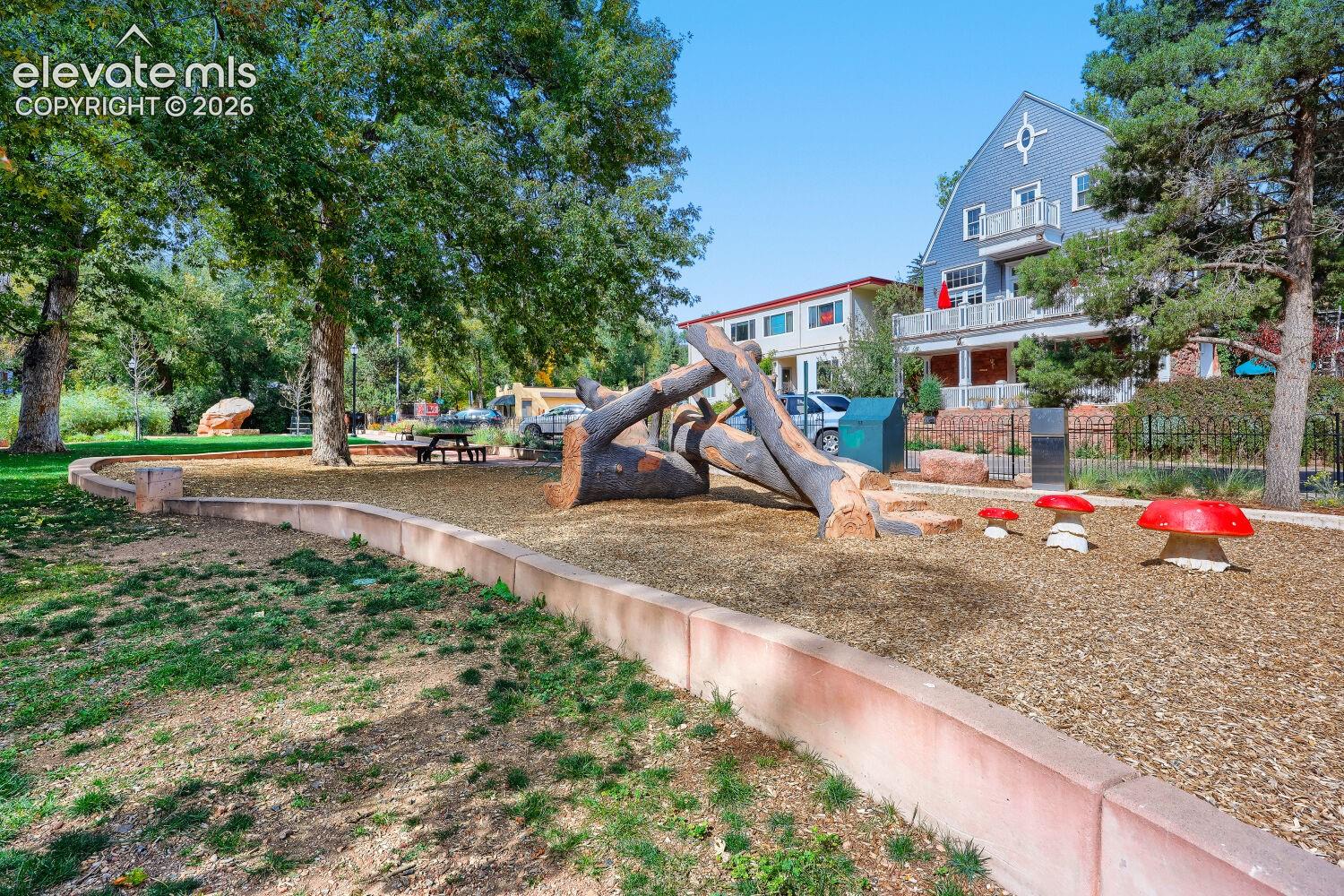 Landscaped outdoor area featuring natural wood play elements, decorative mushroom accents, and mature trees