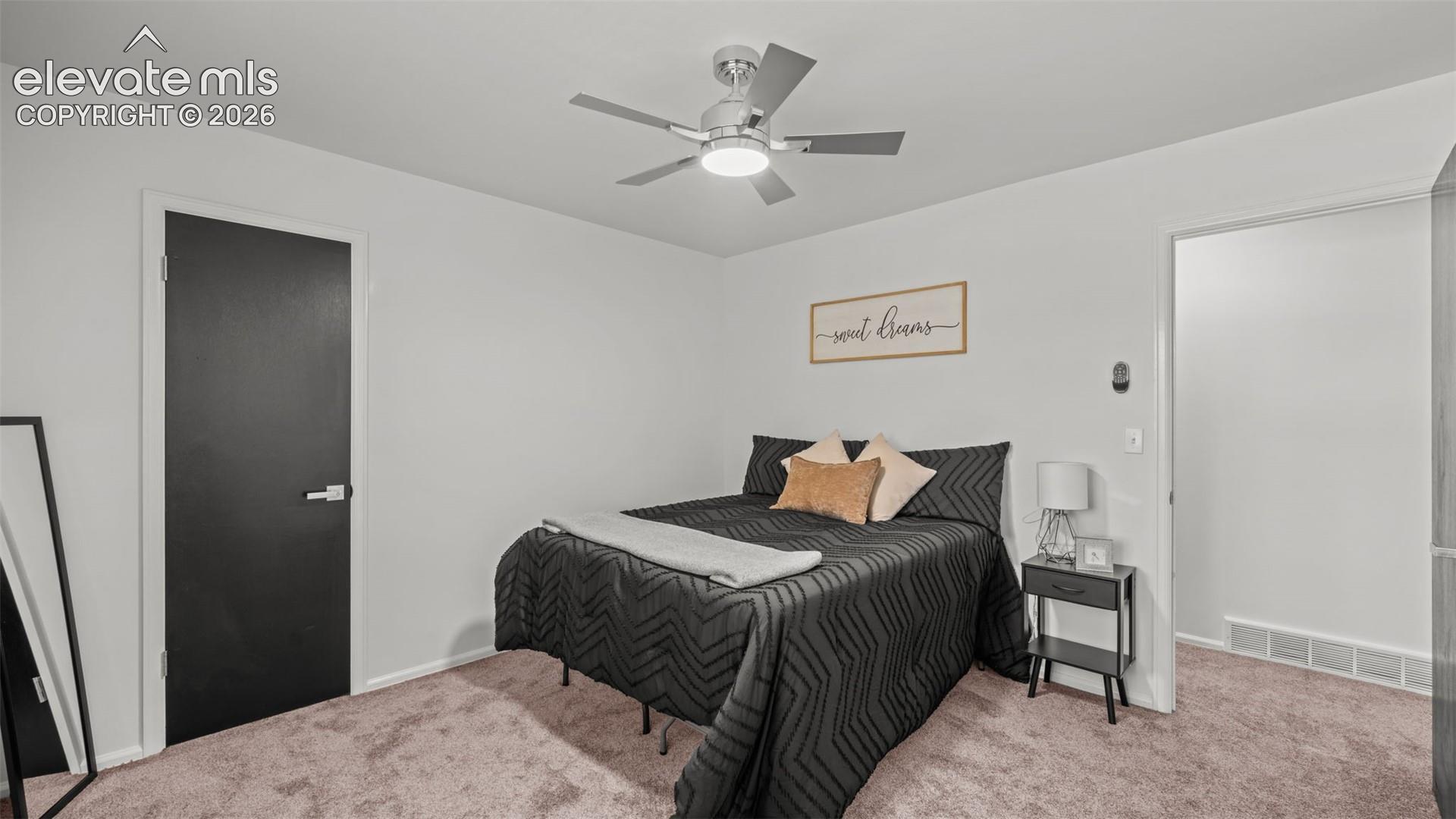 Light-toned walls, ceiling fan with integrated lighting, dark interior door with contemporary hardware, and plush carpeting