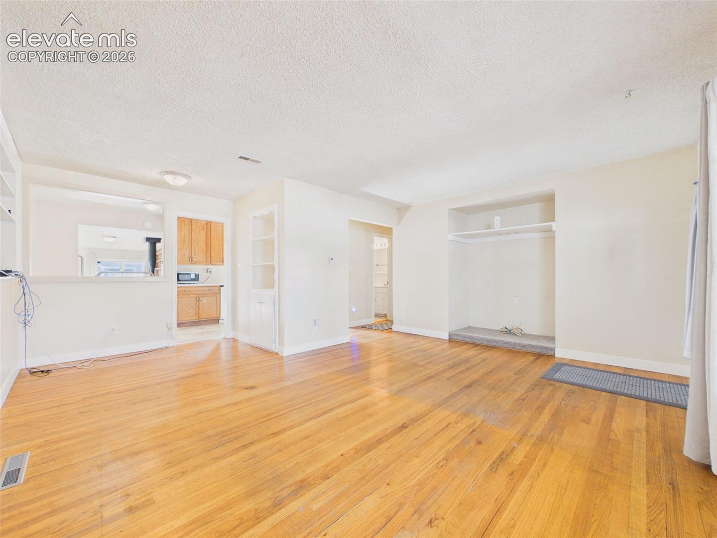 Open living and dining space with original-style hardwood flooring, built-in shelving, and convenient access to the kitchen and hallway.