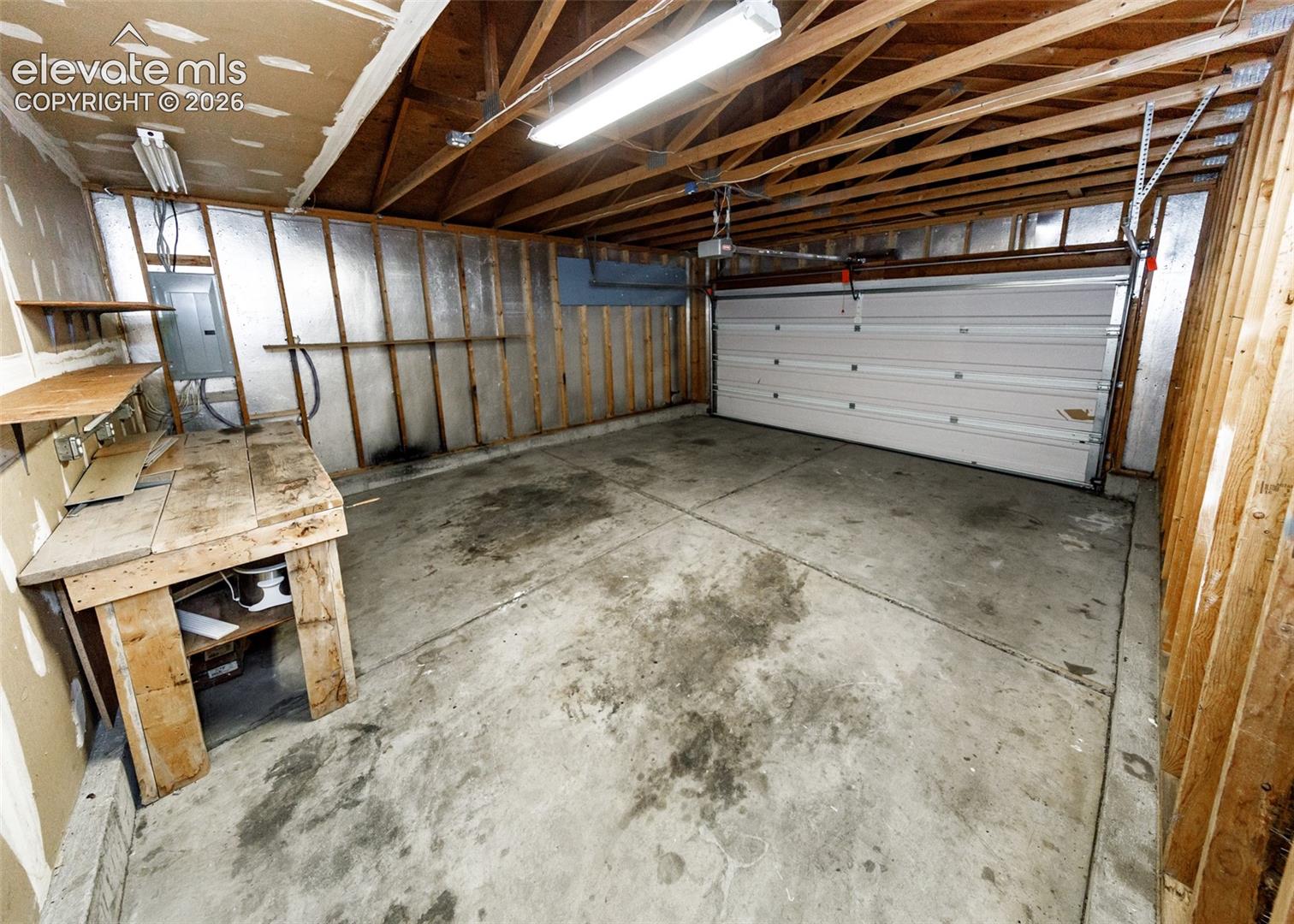 Garage space featuring a concrete floor, built-in wooden workbench, exposed stud framing, and a sectional overhead door