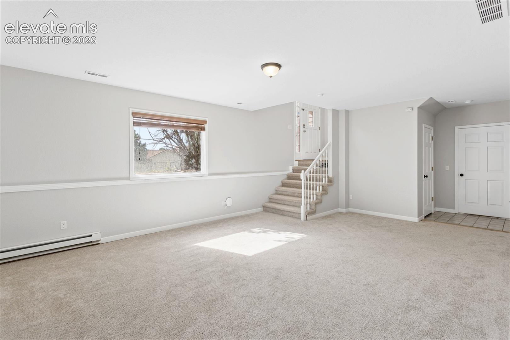 Expansive carpeted area, neutral wall tones, window with natural light, built-in staircase, and a tile entry