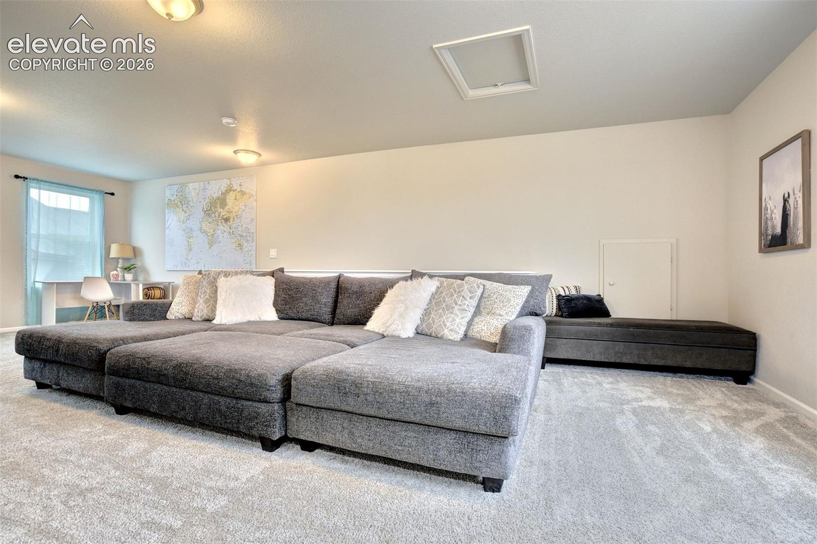 Neutral-toned interior space featuring light-colored wall-to-wall carpeting, dual flush-mount ceiling light fixtures, and a recessed wall panel access door