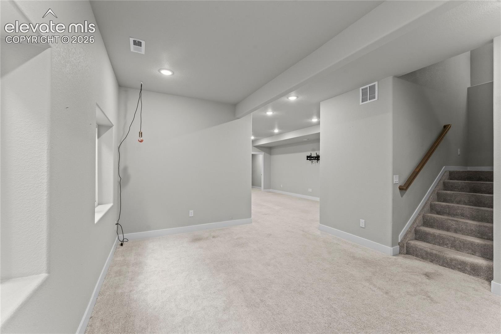 Expansive carpeted area with recessed lighting, a window, and a staircase featuring a wood handrail