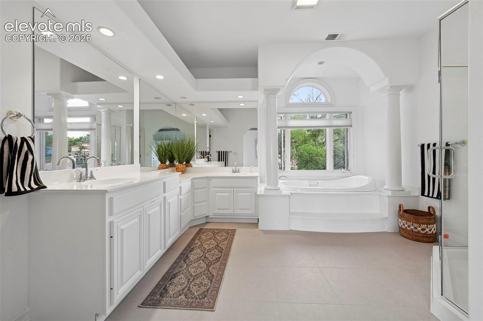 Spacious bathroom featuring a built-in soaking tub, arched window, and dual vanity with extensive counter space