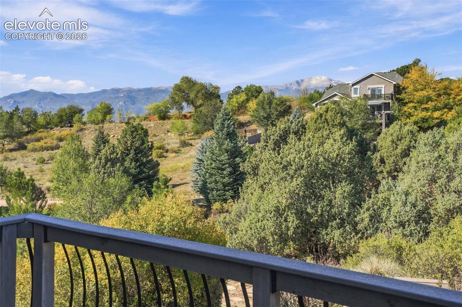 Elevated wood-finish deck with metal spindle railing overlooking a landscape featuring mature pine trees and a mountain range backdrop