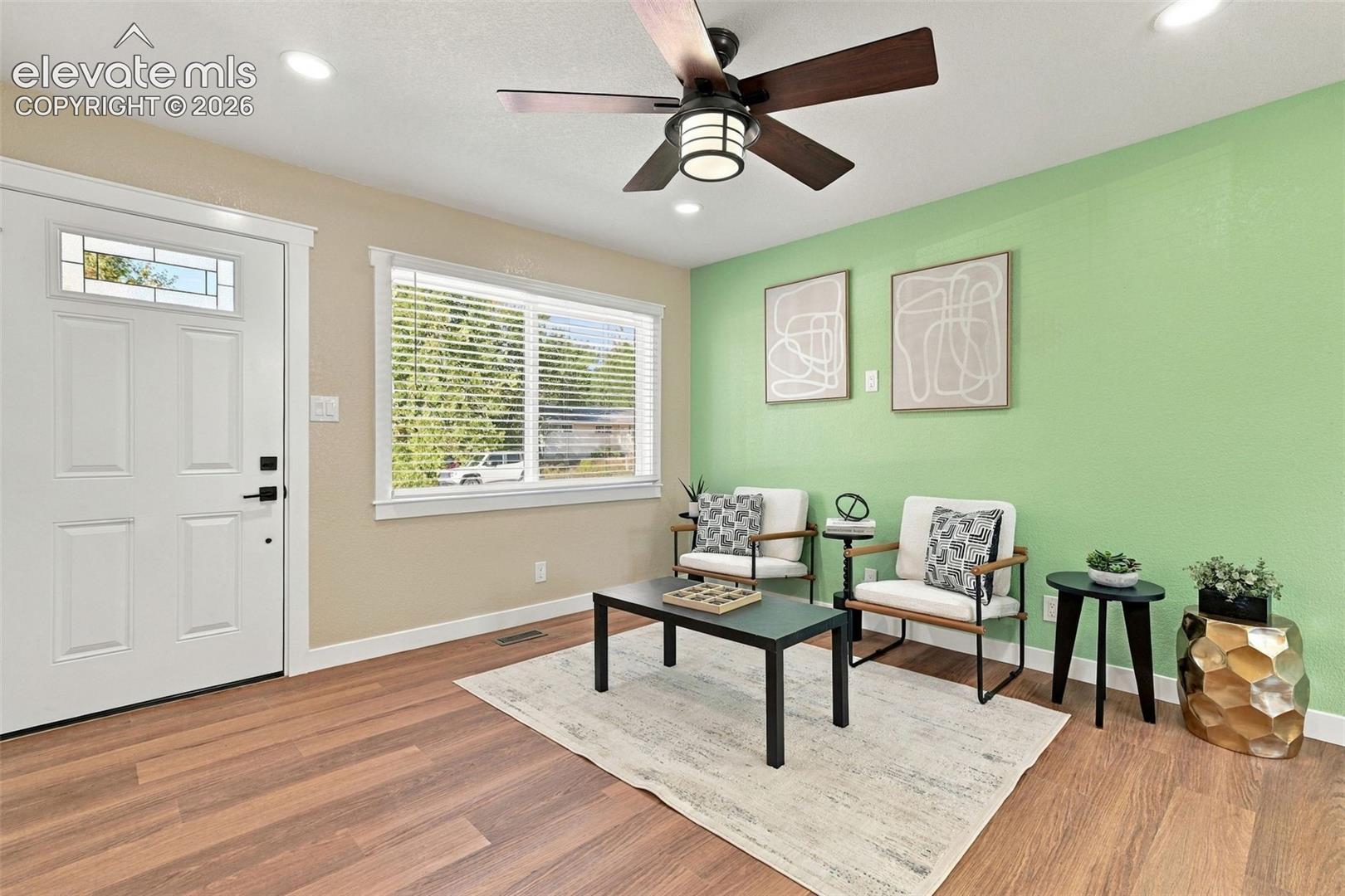Wood-finish flooring, white paneled entry door with transom window, ceiling-mounted paddle fan with integrated lighting, and recessed ceiling lights