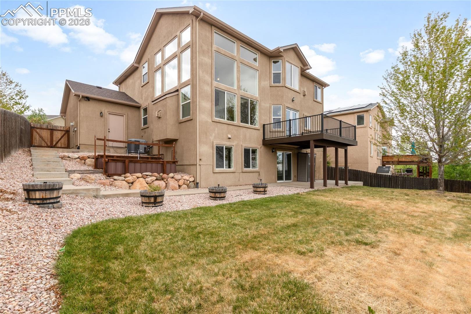 Multi-level exterior featuring a stucco facade, an upper-level deck with black railings, and a ground-level patio