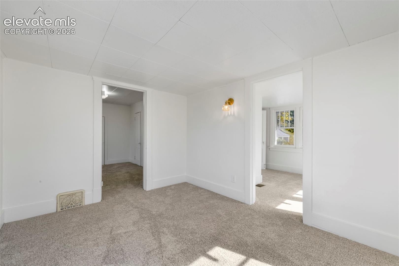 Neutral interior room with wall-to-wall carpeting, paneled ceiling, and wall-mounted brass sconce lighting