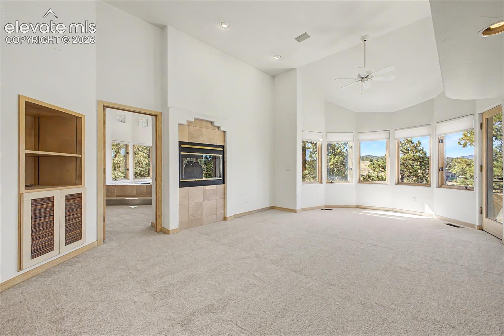Vaulted ceilings, a built-in fireplace with tile surround, an integrated ceiling fan, and built-in shelving with cabinetry