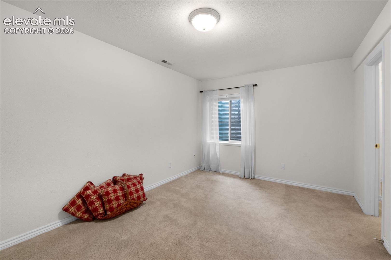 Neutral-toned carpeted flooring, white walls, and a single-window configuration featuring a horizontal-slat window covering and a ceiling-mounted light fixture