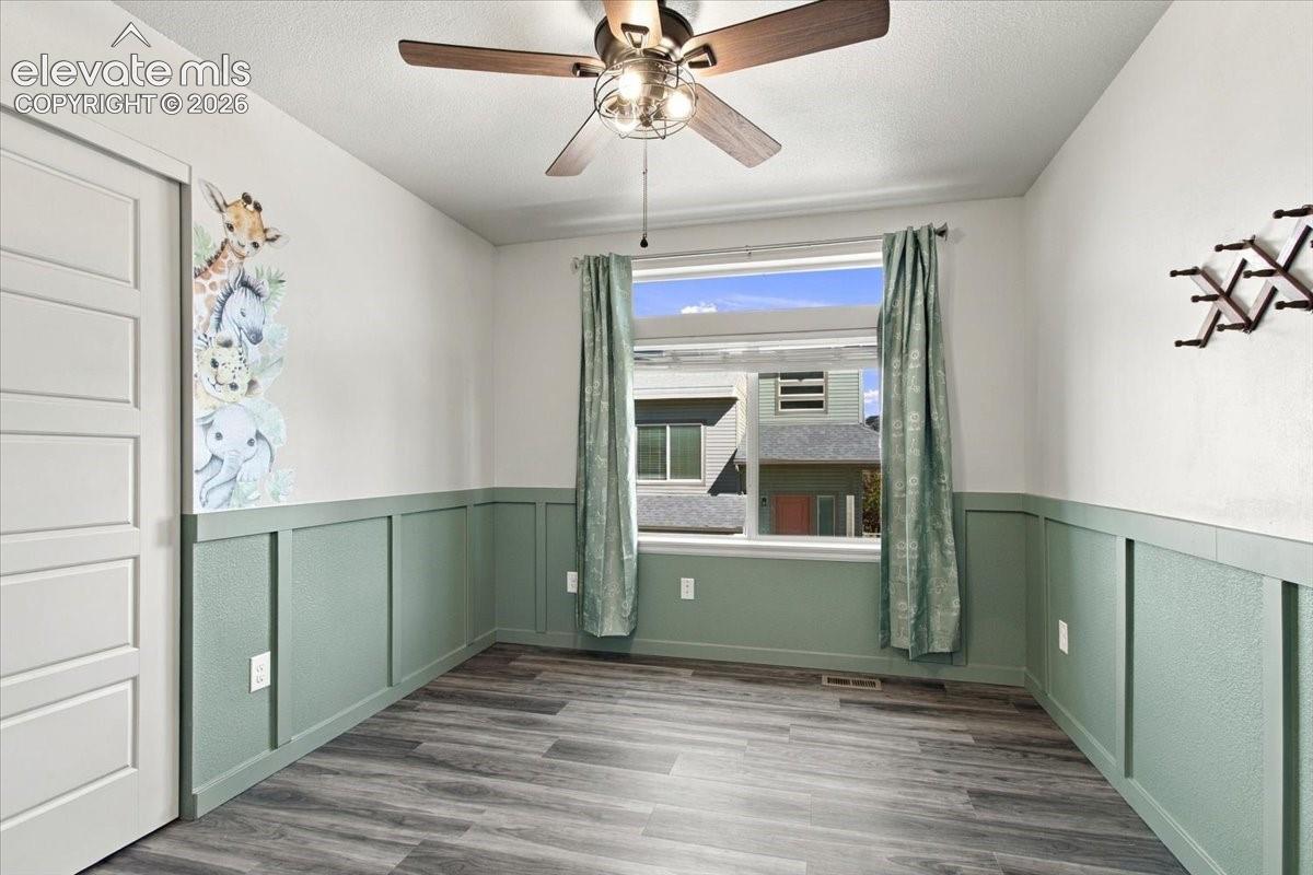 Wood-finish flooring, half-wall wainscoting, white interior door, and a ceiling fan with integrated lighting