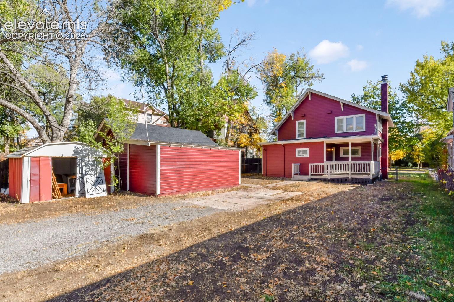 Exterior featuring a detached garage, a secondary storage structure, a covered porch, and a gravel driveway