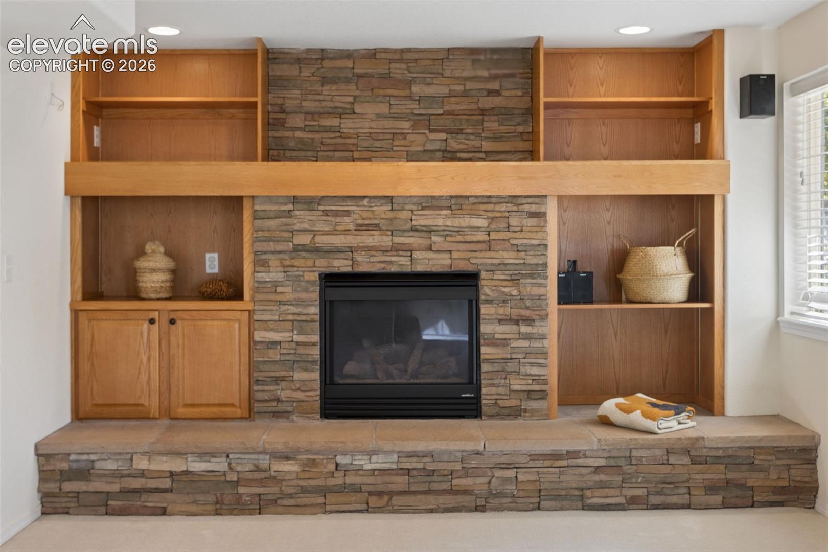 Beautiful stone-faced gas fireplace featuring raised hearth, wood mantel, stone facing and built-in wood shelving