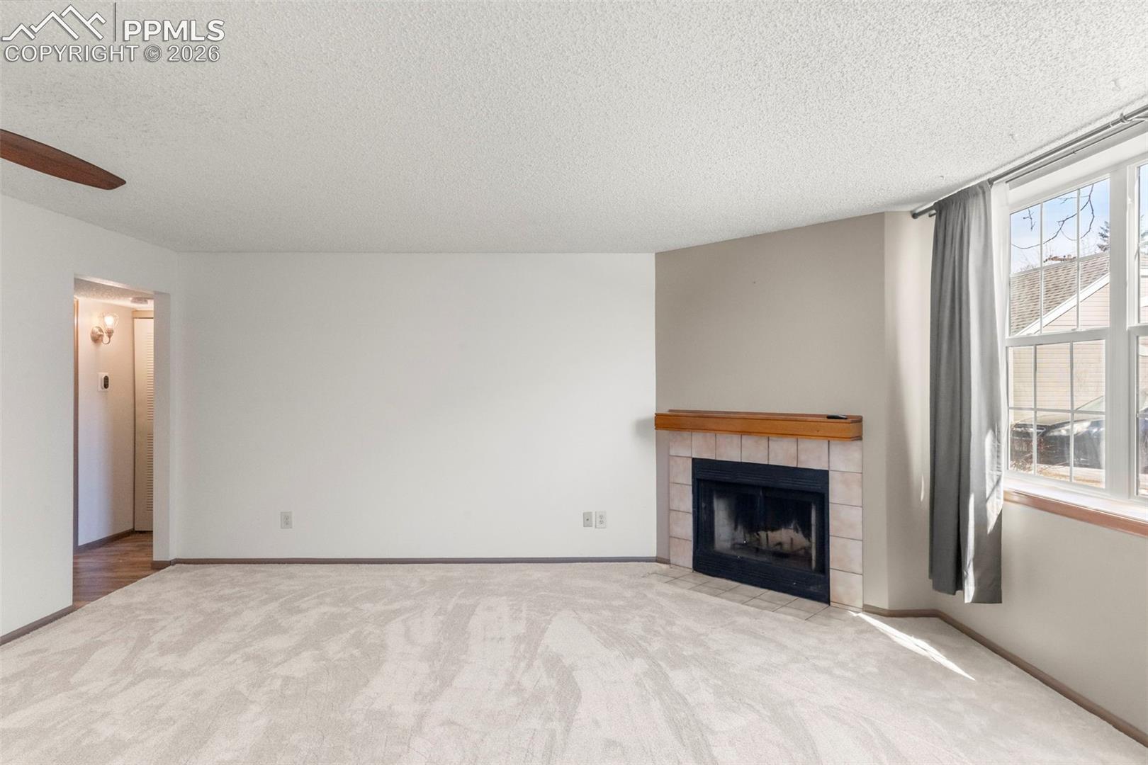 Unfurnished living room with a fireplace, light carpet, ceiling fan, and a textured ceiling