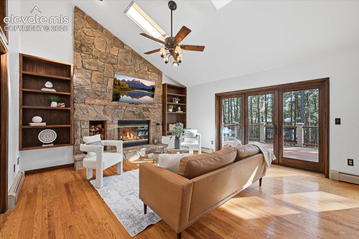 Vaulted ceilings with skylights, stone-faced fireplace, built-in shelving, wood-finish flooring, and glass panel doors to a deck