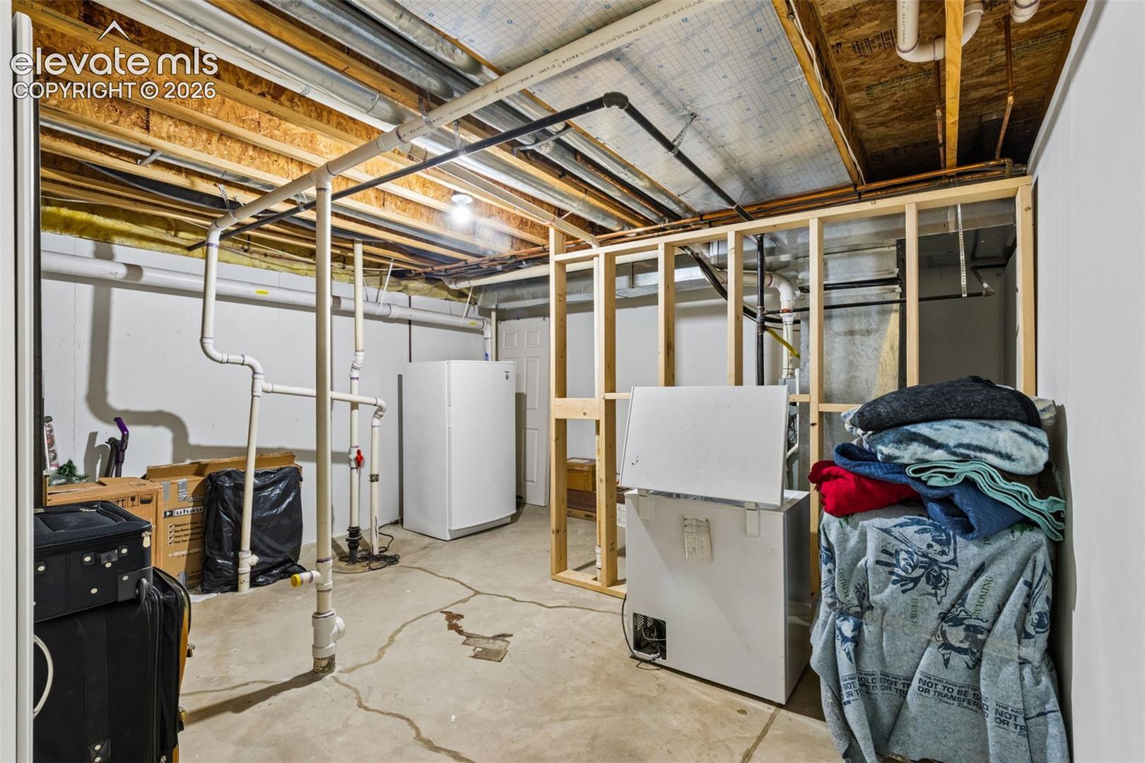 Unfinished utility space featuring concrete flooring, exposed ceiling joists, and wood-framed partition walls